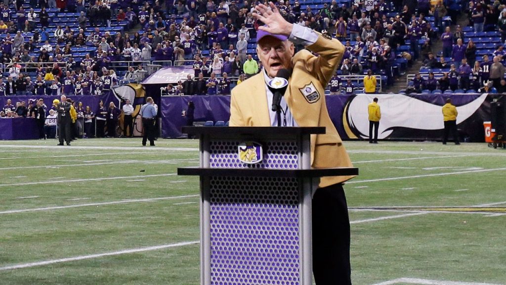 Bud Grant waving to crowd, at podium on football field