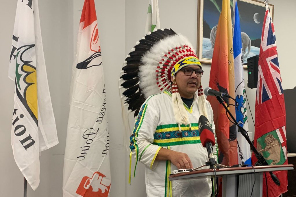 man wearing traditional Indigenous headdress speaking at podium